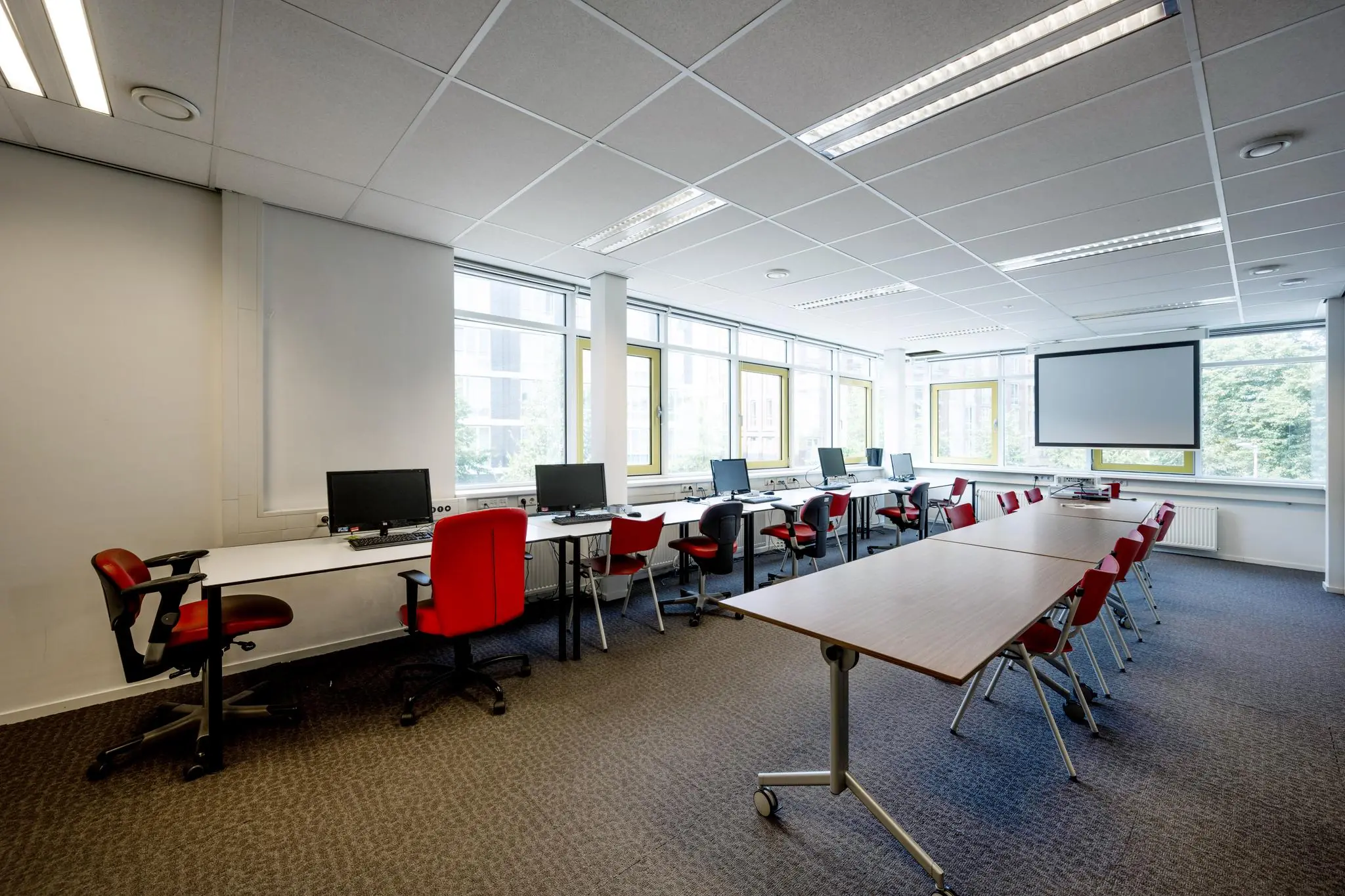 Leslokaal aan de Jan Tooropstraat met computers, rode stoelen en een projectiescherm.